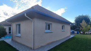 Ein eingeschossiges Haus mit einer gefliesten Terrasse, einem Swimmingpool und einem gepflegten Rasen.