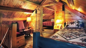 A cozy attic bedroom with a wooden ceiling, a bed with a quilt, a chair, a desk, and a lamp. - Poconos Log Cabin Getaway (Lehighton)
