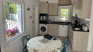 A compact kitchen with a washing machine, dishwasher, and a dining area with a table and chairs. - Charming, renovated house—4-minute walk to Grifeu Beach—Beautiful garden—Parking—Air conditioning (Llançà)