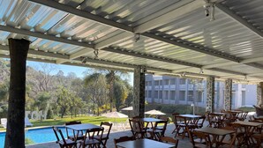 Une terrasse extérieure avec des tables et des chaises, une piscine et une vue sur un immeuble doté de balcons.