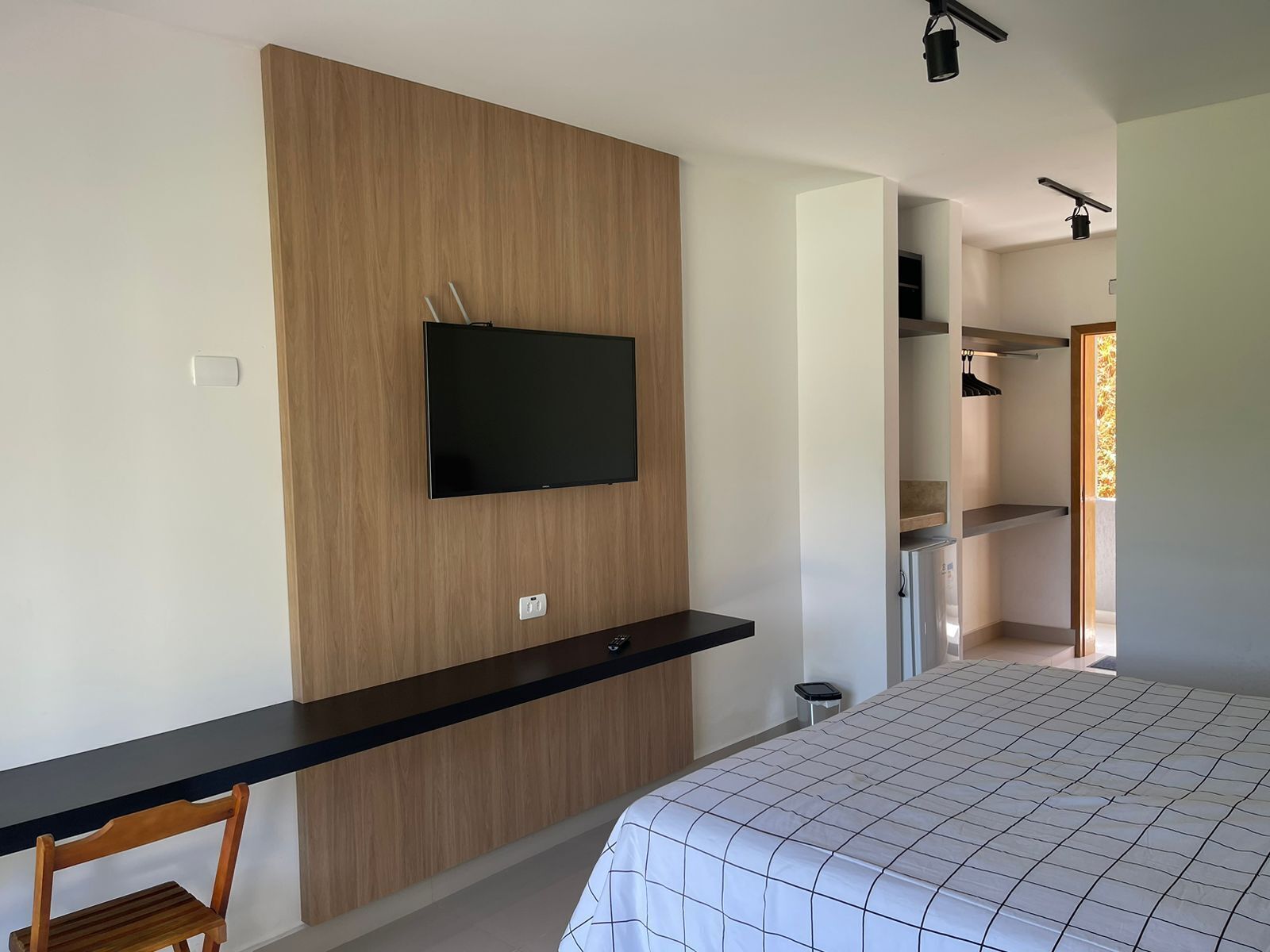 Quarto com cama, televisão fixada em parede de madeira, escrivaninha com cadeira e closet espaçoso.