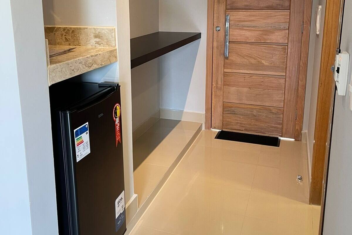 Un pasillo con un refrigerador negro, una puerta de madera y un perchero negro en una pared blanca.