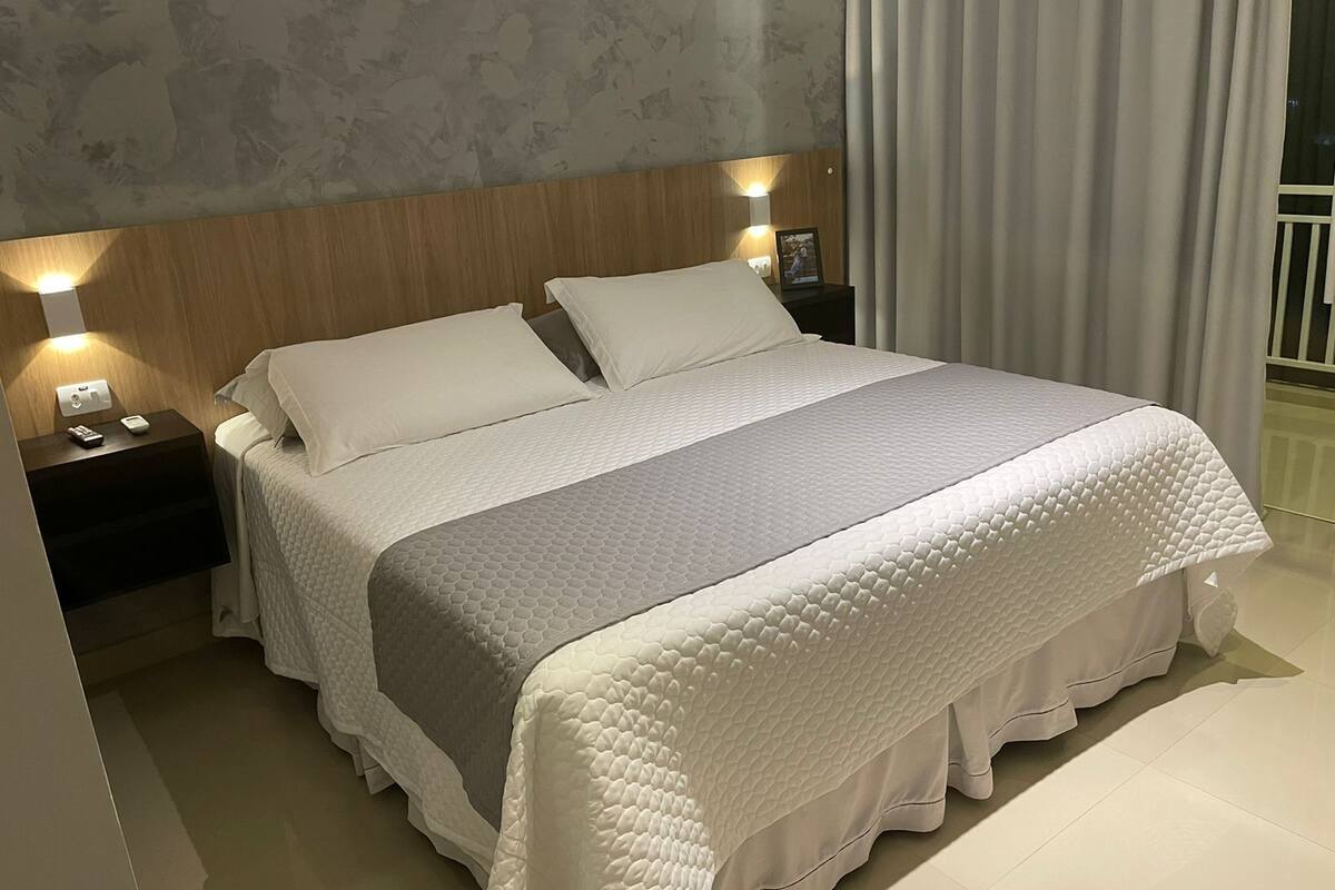 Una cama bien hecha con cubrecolcha acolchado, cabecera de madera y lámparas de noche.