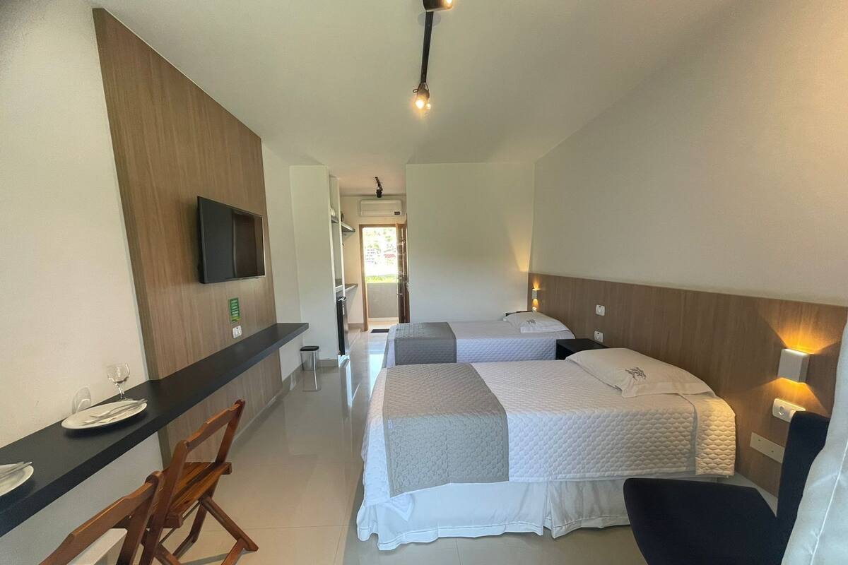 Habitación de hotel con dos camas, un escritorio con sillas, un televisor y un cubo de basura pequeño.