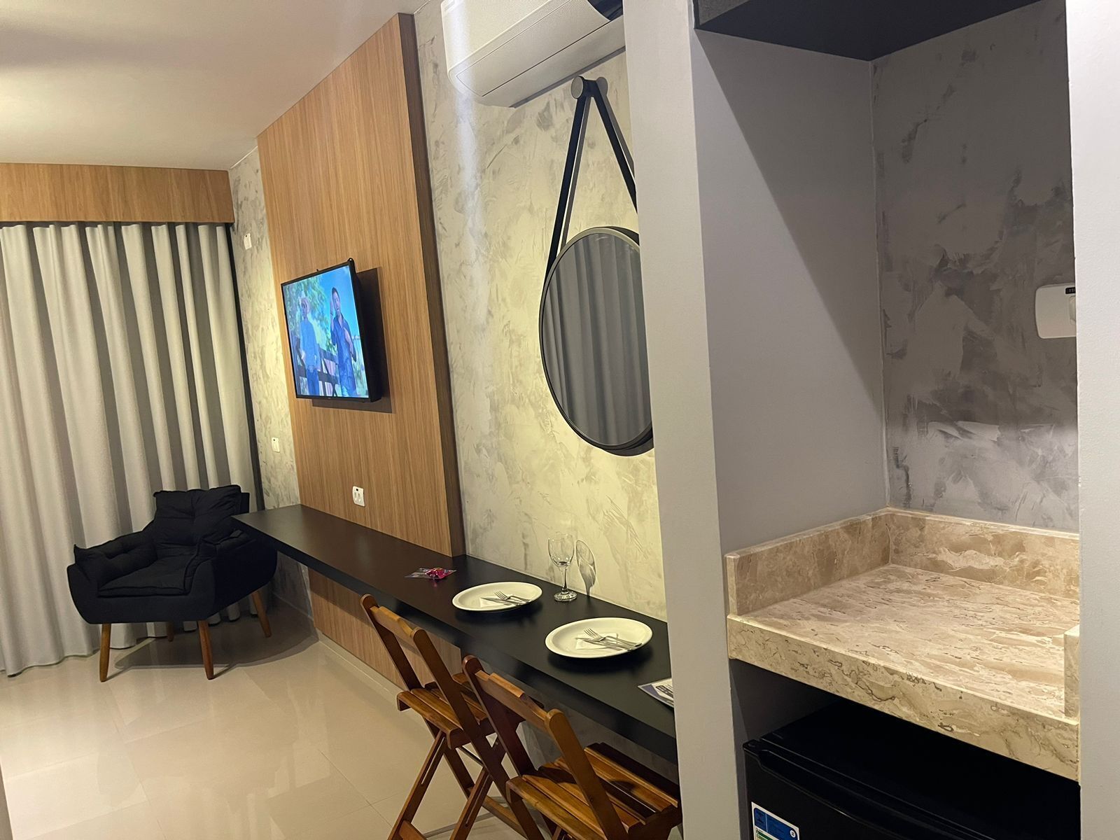A modern kitchen with a marble countertop, a dining table with chairs, a TV mounted on the wall, and a hanging bag.