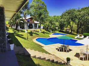 Un patio trasero con piscina, mobiliario exterior y una casa con porche cubierto.