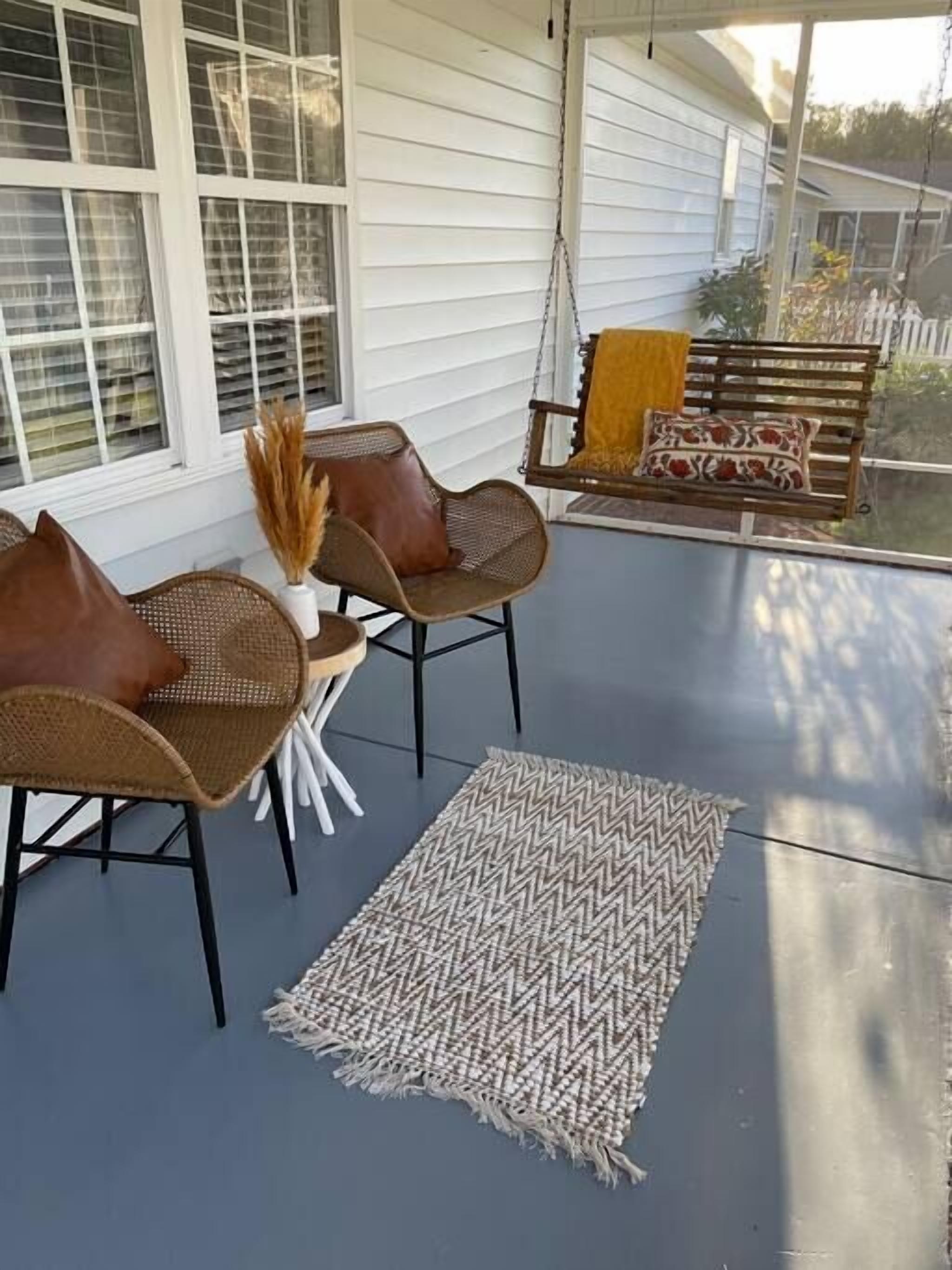 A covered porch with wicker furniture, a swing, and a patterned rug.