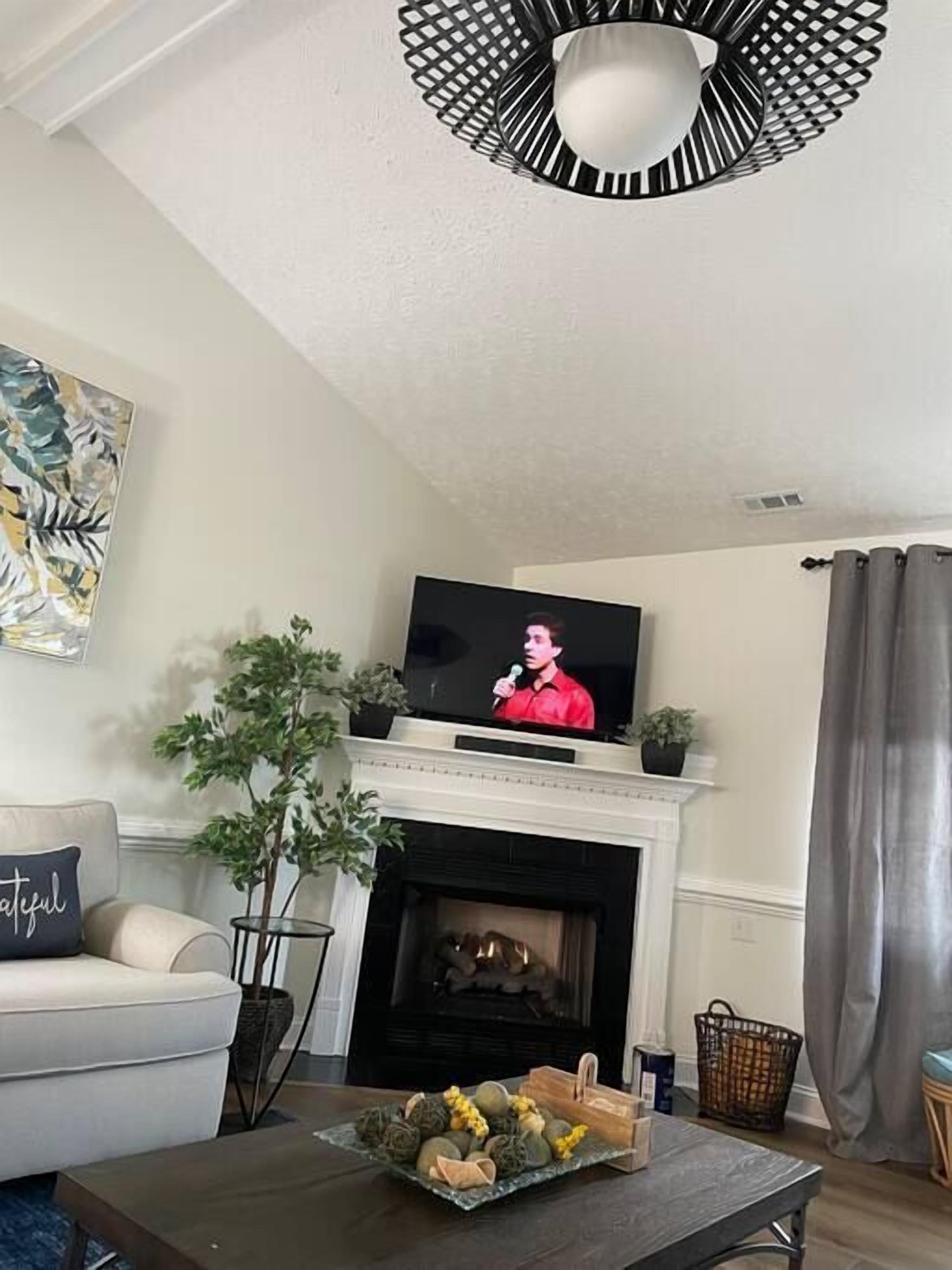 A living room with a fireplace, a television on a mantel, a sofa, and a coffee table with decorative items.