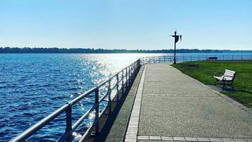 A waterfront promenade with a metal railing, a paved walkway, a bench, and a lamp post.