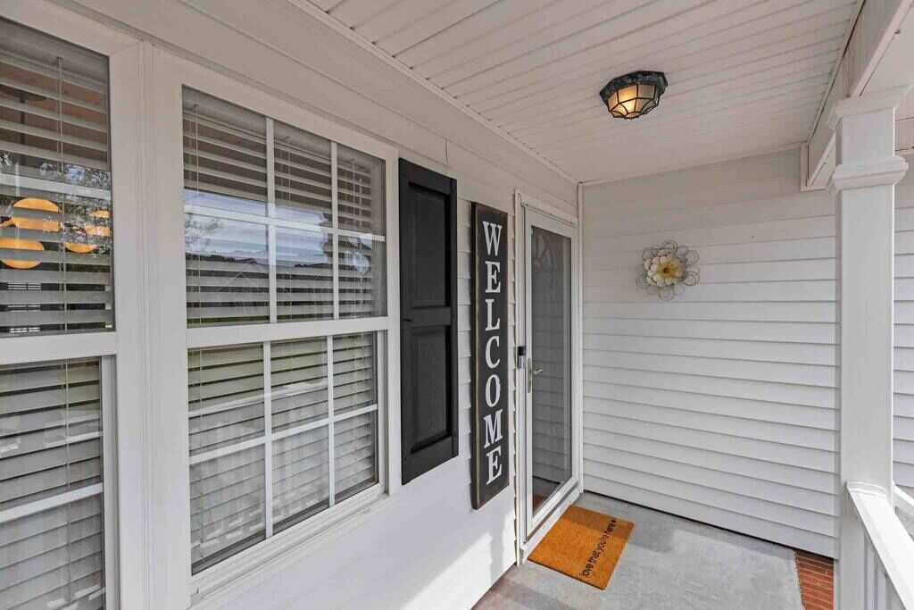 A white exterior with a 'WELCOME' sign, a doormat, and a flower decoration.