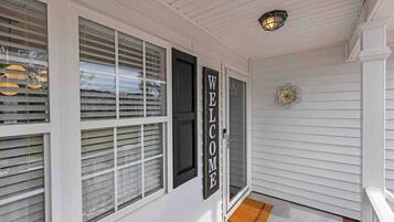 A white exterior with a 'WELCOME' sign, a doormat, and a flower decoration.
