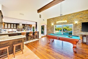 A spacious living area with a pool table, a kitchen with dark wood cabinets, and a stone accent wall.