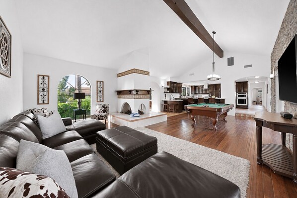 A spacious living room with a pool table, a leather sofa, and a kitchen area with a dining table.