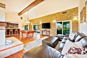 A spacious living area with a pool table, leather sofa, and a stone wall.