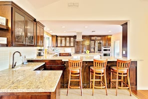 A kitchen with a large island, wooden bar stools, stainless steel appliances, and a tiled backsplash. - Great Reviews w/ 7 Beds, Pool, Hot Tub & Fire Pit! (Temecula)
