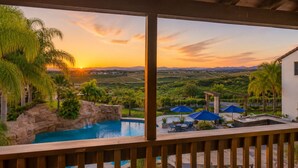 Una piscina con cascada, mobiliario exterior y vistas a un atardecer sobre un paisaje.