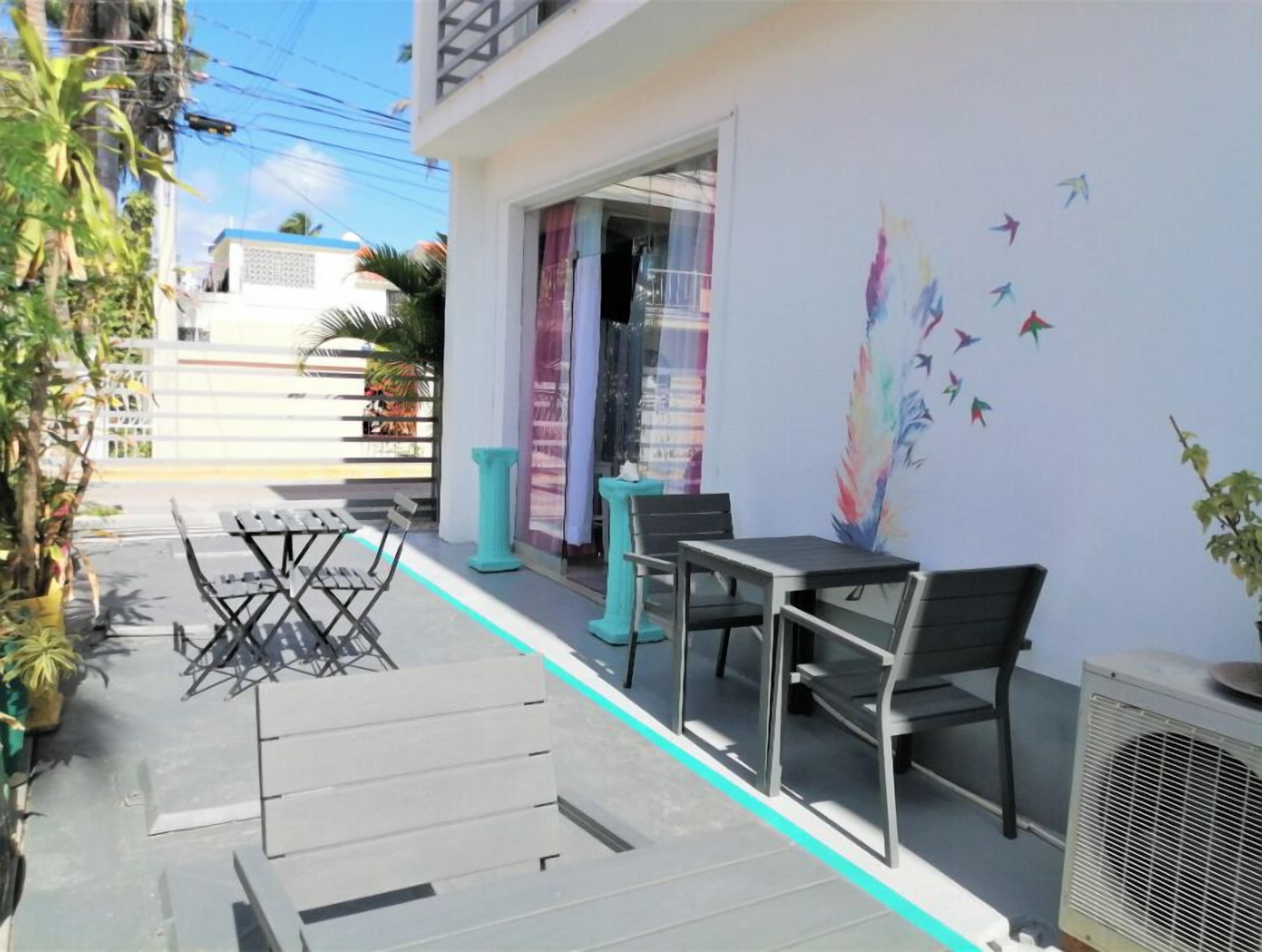 An outdoor seating area with tables and chairs, a mural on the wall, and a building entrance.
