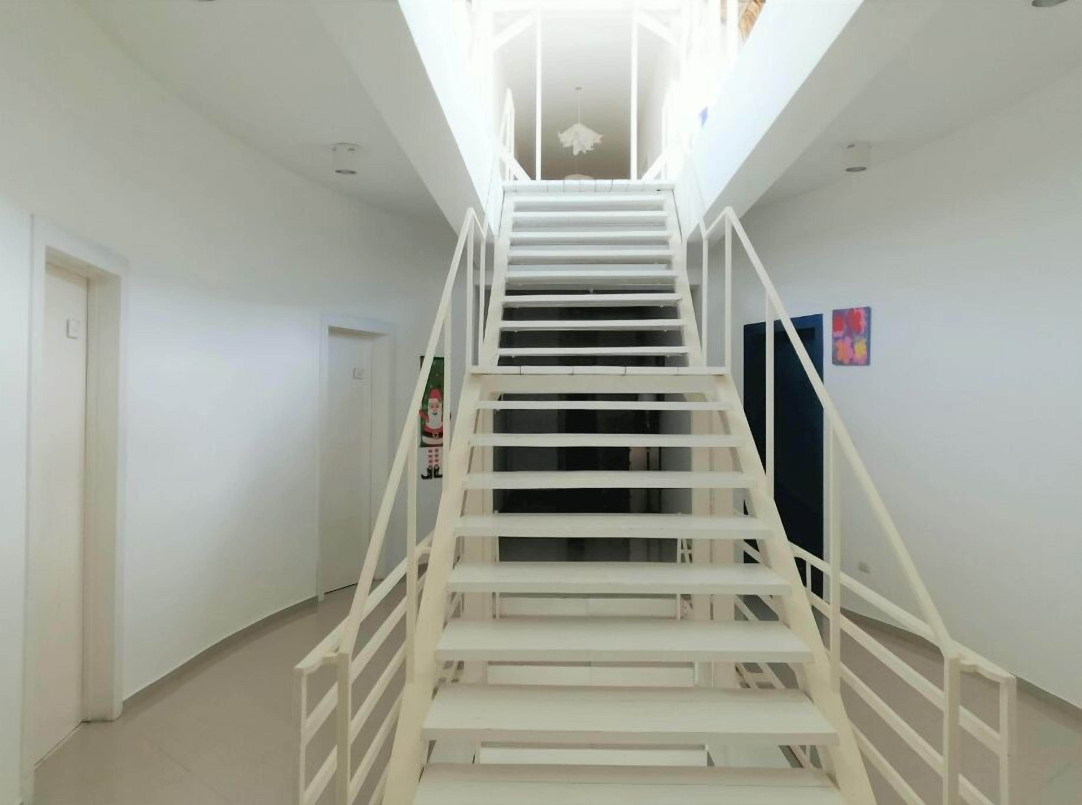 Uma escada branca com corrimão, que leva a um patamar com luminária no teto.
