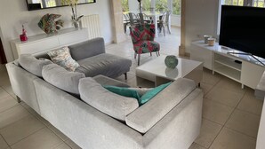 Una sala de estar moderna con un sofá gris, una mesa de centro, un televisor y una zona de comedor con sillas y una mesa.