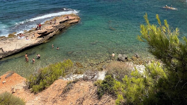 Un paisaje costero con aguas transparentes, acantilados rocosos y vegetación escasa.