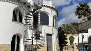 Un edificio blanco con escalera espiral, piscina y palmeras.