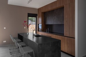 Une cuisine moderne dotée d’un îlot central, de tabourets de bar, d’un four encastré et d’un mur d’accent en pierre.