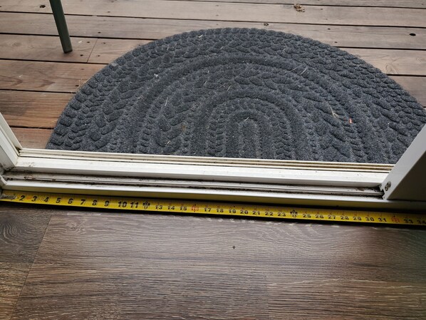 A doormat on a wooden deck with a measuring tape placed across it.