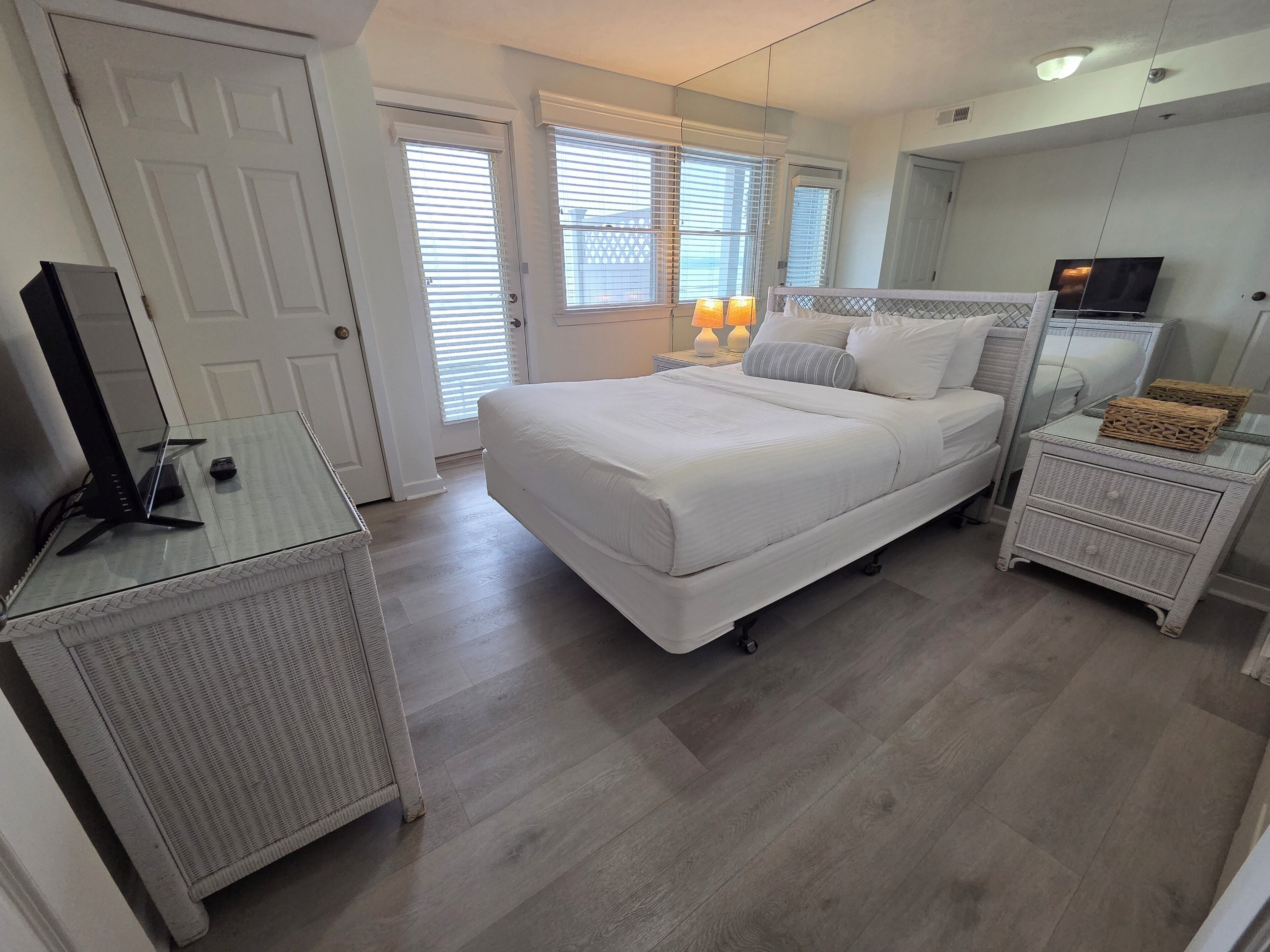A bedroom with a bed, bedside tables, a TV, and a window with blinds.