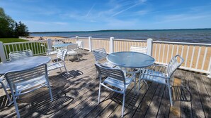 A wooden deck with white metal furniture overlooking a lake. - Beachfront Bliss! - North Shore Inn Unit 103 (Traverse City)