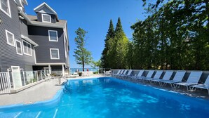 A swimming pool with lounge chairs, a building with a balcony, and trees in the background. - Beachfront Bliss! - North Shore Inn Unit 103 (Traverse City)