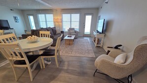 A living room with a round dining table, chairs, a sofa, a coffee table, and a TV. - Beachfront Bliss! - North Shore Inn Unit 103 (Traverse City)