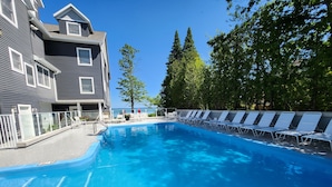 Ein Swimmingpool mit Liegestühlen, ein Gebäude mit Balkon und Bäume im Hintergrund.