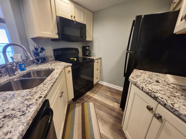 A kitchen with white cabinets, a black microwave, a black stove, a black refrigerator, and a striped rug.