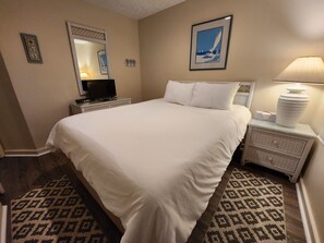 A hotel room with a large bed, a nightstand with a lamp, a dresser, and a mirror. - The Beach Awaits! Updated Kitchen - North Shore Inn Condo 208 (Traverse City)