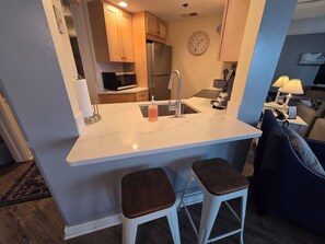 A compact kitchen with a central island, a microwave, a refrigerator, and a clock on the wall. - The Beach Awaits! Updated Kitchen - North Shore Inn Condo 208 (Traverse City)