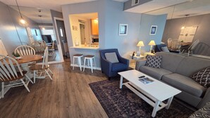 Ein modernes Wohnzimmer mit Essbereich, einer Couch, einem Couchtisch und einer Küche im Hintergrund.
