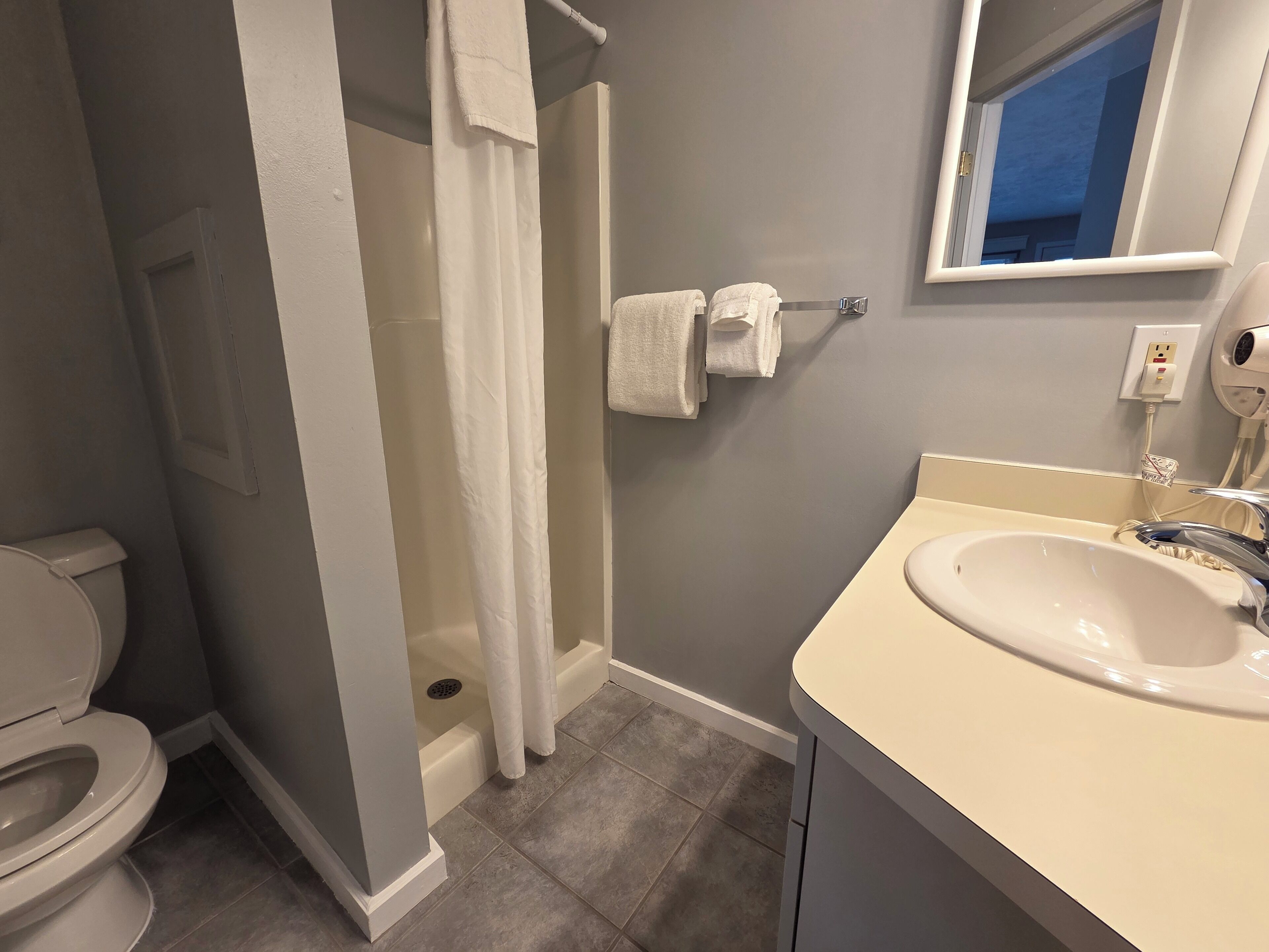 Un baño con inodoro, ducha, lavamanos y perchero para toallas.