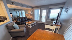 A living room with a sofa, armchair, coffee table, and dining table. - Northern Michigan Charm, North Shore Inn Condo 209 (Traverse City)