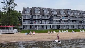 A multi-story hotel with balconies, a beach area with sun loungers, and a water body in the foreground. - Northern Michigan Charm, North Shore Inn Condo 209 (Traverse City)
