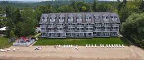 Ein großes, mehrstöckiges Hotel mit symmetrischer Fassade, mehreren Balkonen und einem Strandbereich mit Liegestühlen.