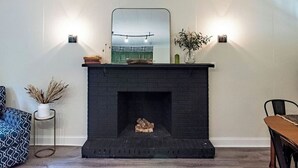 Ein modernes Wohnzimmer mit schwarzem Kamin, einem großen Spiegel darüber und einem Essbereich mit Holztisch und Stühlen.