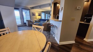 Een eetgedeelte met een houten tafel en stoelen, een keuken met een bar en een woonkamer met een bank en fauteuils.