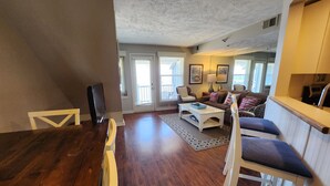 A spacious living room with a wooden dining table, a sofa, and a coffee table. There is a door leading to a balcony. - Top Floor, Private Master Suite, 2 Balconies - North Shore Inn Condo 304 (Traverse City)