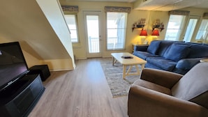 A living room with a flat-screen TV, a blue sofa, a coffee table, and a staircase. - Stunning Views, Private Master Suite - North Shore Inn Condo 306 (Traverse City)