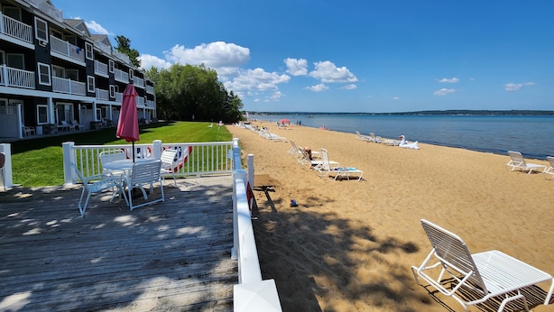 A beach with white lounge chairs and a wooden deck with white railings. - Stunning Views, Private Master Suite - North Shore Inn Condo 306 (Traverse City)