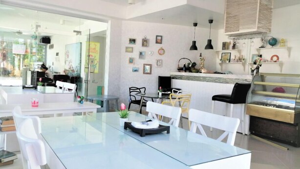 Zona pranzo moderna con tavoli in vetro e sedie bianche, cucina con bancone e diversi elementi decorativi alle pareti.
