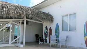 Un'area esterna riparata con tetto in paglia, pareti bianche e tavole da surf esposte.