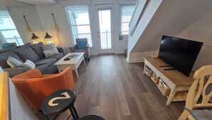 A modern living room with a sofa, chairs, a coffee table, a TV, and a staircase. - Sunsets Await in 308! 2 Bayside Balconies - North Shore Inn Condo 308 (Traverse City)