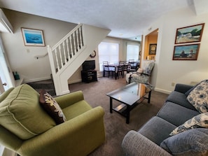 A living room with a staircase, a dining area, and a view of the ocean.