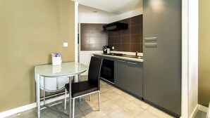 A compact kitchen with a dining table and chairs, a built-in oven, and a microwave. - Florella Residences 2 pièces duplex Achard (Cannes)